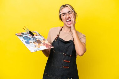 Sarı arka planda izole edilmiş palet tutan beyaz bir kadın ağzı açık bağırıyor.