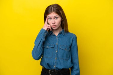 Sarı arka planda izole edilmiş genç bir İngiliz kadın bir fikir düşünüyor.