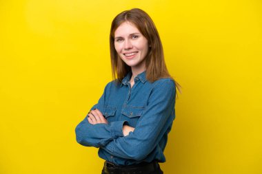 Sarı arka planda izole edilmiş, kolları çapraz ve ileriye bakan genç bir İngiliz kadın.