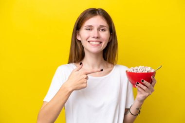 Sarı arka planda izole edilmiş bir fincan kahve tutan genç İngiliz kadın.