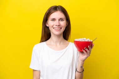 Sarı arka planda izole edilmiş bir fincan kahve tutan genç İngiliz kadın çok gülümsüyor.