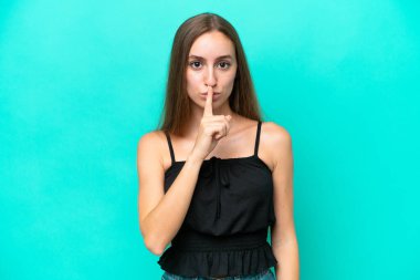 Mavi arka planda izole edilmiş beyaz bir kadın sessiz bir jest işareti gösteriyor. Parmağını ağzına sokuyor.