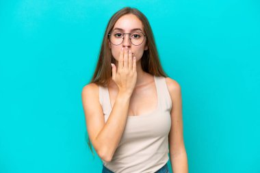 Mavi arka planda izole edilmiş, ağzı elle kaplanmış beyaz bir kadın.