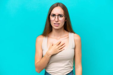 Mavi arka planda izole edilmiş genç beyaz kadın kendini işaret ediyor.
