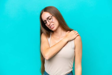 Genç, beyaz bir kadın mavi arka planda izole edilmiş. Omuz ağrısı çekiyor. Çabaladığı için.