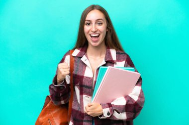 Mavi arka planda izole edilmiş genç beyaz kadın galibiyeti kutluyor.