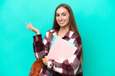 Genç beyaz kadın, mavi arka planda izole edilmiş. Davet etmek için ellerini yana uzatıyor.