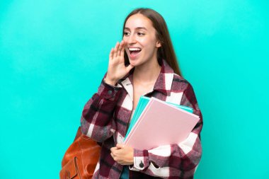 Mavi arka planda izole edilmiş genç beyaz kadın ağzı sonuna kadar açık bağırıyor.