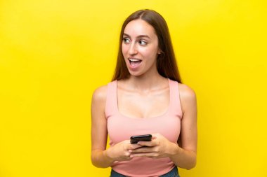 Young caucasian woman isolated on yellow background using mobile phone and looking up