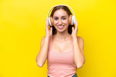 Sarı arka planda izole edilmiş genç beyaz kadın müzik dinliyor.