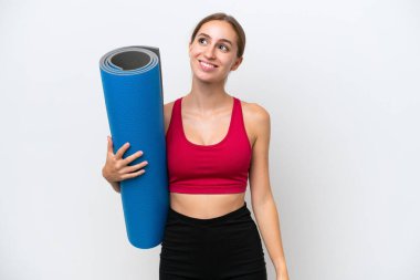 Beyaz arka planda izole edilmiş bir minderi tutarken yoga derslerine giden beyaz bir kadın yukarı bakarken bir fikir düşünüyor.