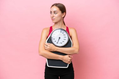 Pembe arka planda izole edilmiş beyaz bir kadın. Tartma makinesi ve bakınıyor.