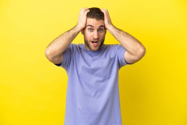 Sarışın yakışıklı adam, izole edilmiş sarı arka planda, gergin hareketler yapıyor.