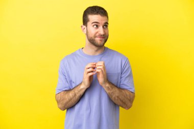 Sarışın yakışıklı adam izole edilmiş sarı arka plan entrikaları çeviriyor.