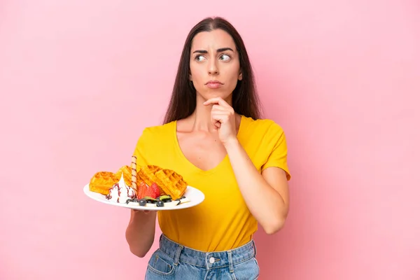 Young Caucasian Woman Holding Waffles Isolated Pink Background Having Doubts — стоковое фото