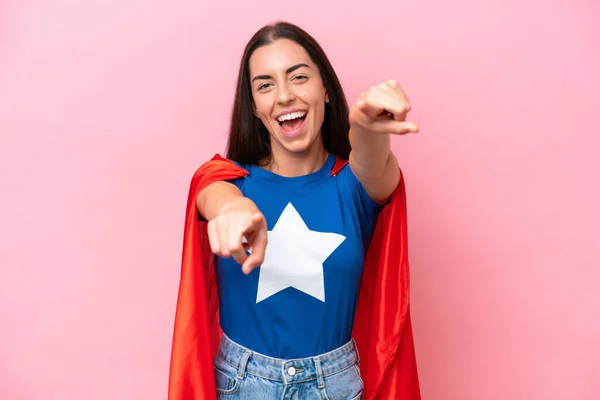 Super Hero Caucasian woman isolated on pink background points finger at you while smiling