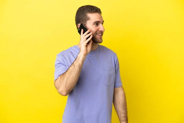 Przystojny Blondyn Nad Odizolowanym Żółtym Tle Prowadząc Rozmowę Telefonem Komórkowym — Zdjęcie stockowe