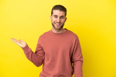 Sarışın yakışıklı, izole edilmiş sarı arka planda. Avucunun içinde bir reklam koymak için hayali mekan tutuyor.