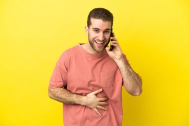 Yakışıklı sarışın adam izole edilmiş arka planda cep telefonu kullanıyor. Çok gülümsüyor.