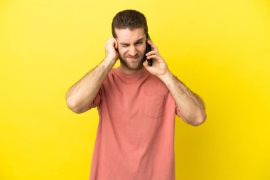 Handsome blonde man using mobile phone over isolated background frustrated and covering ears