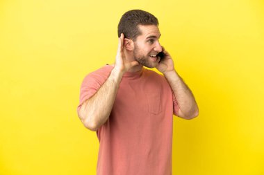 Yakışıklı sarışın adam izole edilmiş arka planda cep telefonu kullanıyor. Kulağına elini sürerek bir şeyler dinliyor.