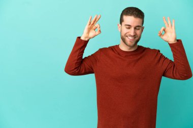 Zen pozunda mavi arka planda yakışıklı sarışın bir adam.