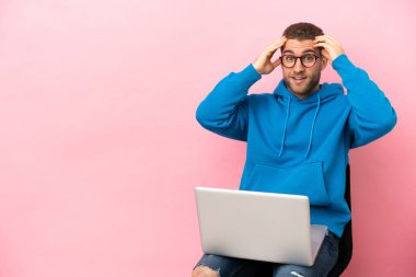 Genç adam dizüstü bilgisayarlı bir sandalyede oturuyor ve şaşırmış görünüyor.