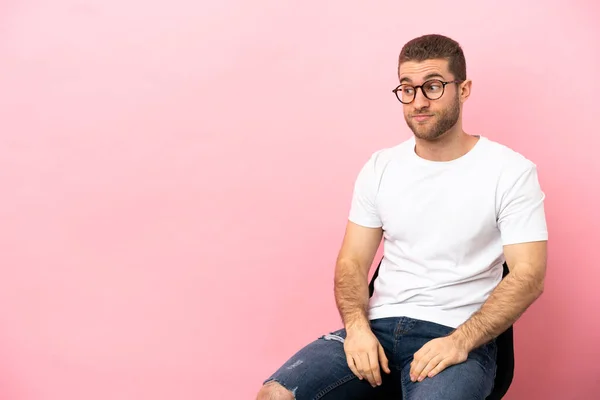 Young Man Sitting Chair Isolated Pink Background Making Doubts Gesture — Foto de Stock