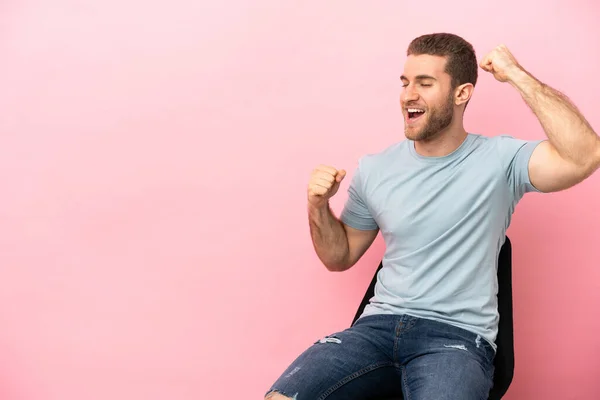 Mladý Muž Sedí Židli Nad Izolované Růžové Pozadí Slaví Vítězství — Stock fotografie