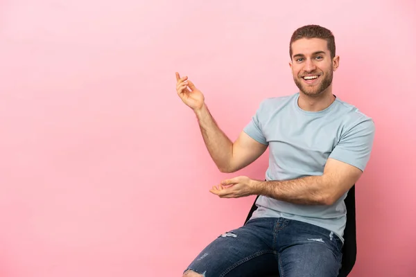 Young Man Sitting Chair Isolated Pink Background Extending Hands Side — Stock fotografie