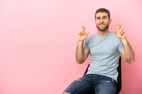 Young Man Sitting Chair Isolated Pink Background Fingers Crossing Wishing — Φωτογραφία Αρχείου