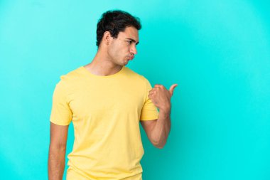 Izole mavi arka plan üzerinde Kafkas yakışıklı adam mutsuz ve yan işaret