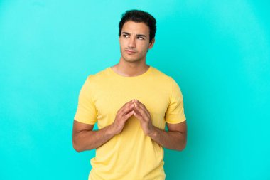 Kafkasyalı yakışıklı adam izole edilmiş mavi arka plan entrikaları çeviriyor.