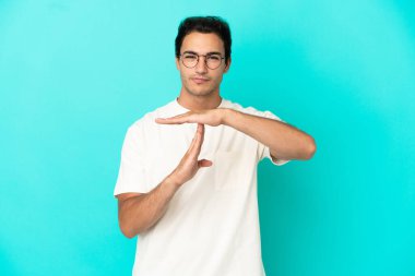 Kafkasyalı yakışıklı adam izole edilmiş mavi arka planda zaman geçirme hareketi yapıyor.