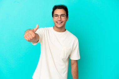Beyaz yakışıklı adam izole mavi arka plan üzerinde başparmak yukarı çünkü iyi bir şey oldu