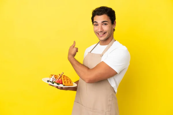 Restaurante Garçom Segurando Waffles Sobre Fundo Amarelo Isolado Apontando Para — Fotografia de Stock