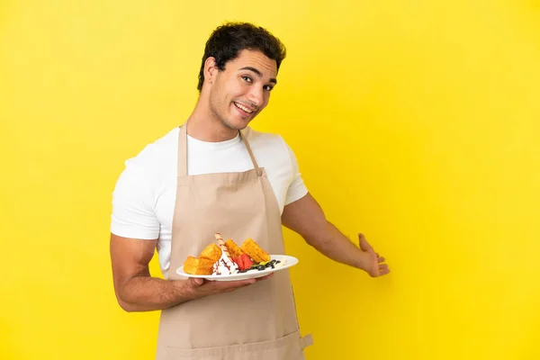 Restaurant Waiter Holding Waffles Isolated Yellow Background Extending Hands Side — Zdjęcie stockowe