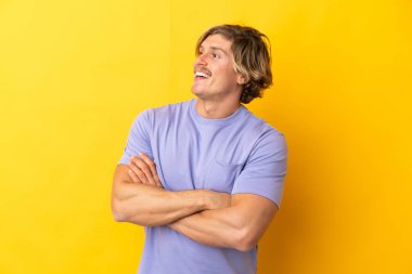 Sarı arka planda izole edilmiş yakışıklı sarışın adam mutlu ve gülümsüyor.