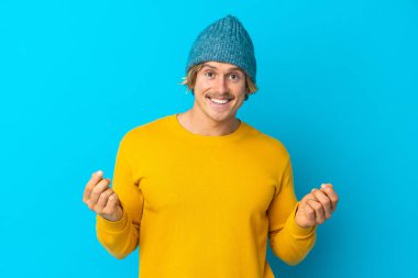 Yakışıklı sarışın adam mavi arka planda izole edilmiş para hareketi yapıyor.