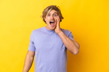 Sarışın yakışıklı adam, sarı arka planda izole edilmiş, şaşırmış ve şok olmuş bir yüz ifadesi var.