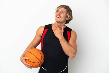 Beyaz arka planda izole edilmiş basketbol topunu tutan genç sarışın adam gülümserken yukarı bakıyor.