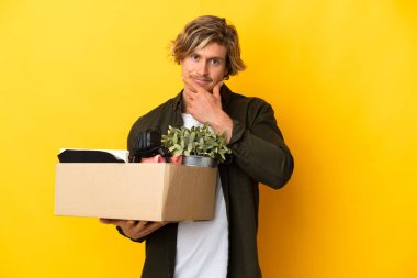 Sarışın adam, sarı arka planda izole edilmiş şeylerle dolu bir kutuyu kaldırırken hamle yapıyor.