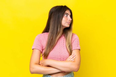 Sarı arka planda izole edilmiş genç beyaz kadın kollarını kavuşturuyor.