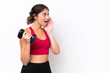 Beyaz arka planda izole haldeyken halter kaldıran genç beyaz kadın ağzı sonuna kadar açık bağırıyor.