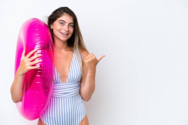 Bembeyaz arka planda izole edilmiş şişme şilte donutu tutan mayo giymiş genç bir kadın bir ürünü sunmak için yan tarafı işaret ediyor.