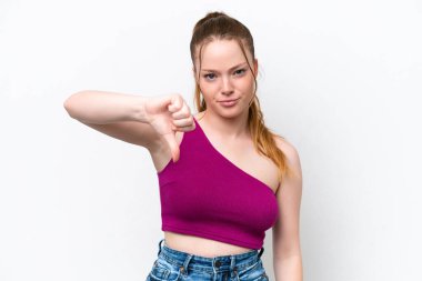 Beyaz arka planda izole edilmiş genç beyaz kız olumsuz ifadeyle baş parmağını aşağı gösteriyor.