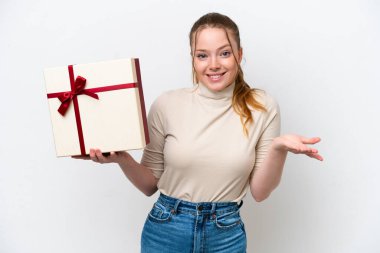 Beyaz arka planda yüzü şoke olmuş genç beyaz bir kadın elinde bir hediye tutuyor.