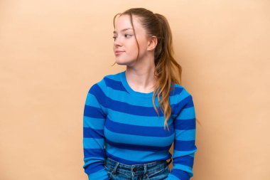 Beyazlı genç bir kadın bej arka planda izole edilmiş, yan tarafa bakıyor.