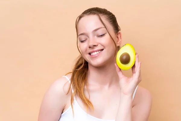 Young Caucasian Girl Isolated Beige Background Holding Avocado While Smiling — Stok fotoğraf