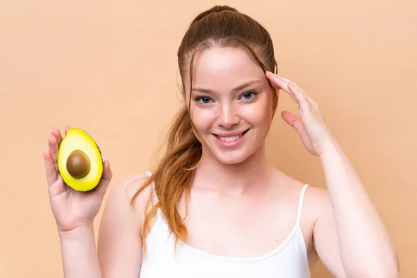 Young Caucasian Girl Isolated Beige Background Holding Avocado While Smiling — Stockfoto
